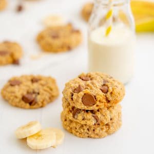 Three thick oat cookies stacked in a tower next to slices of banana.