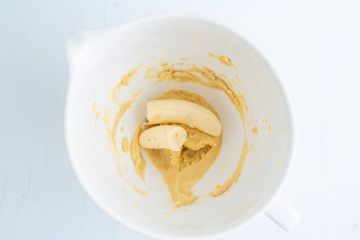 A white ceramic mixing bowl with creamed butter and sugar and a banana broken in half.