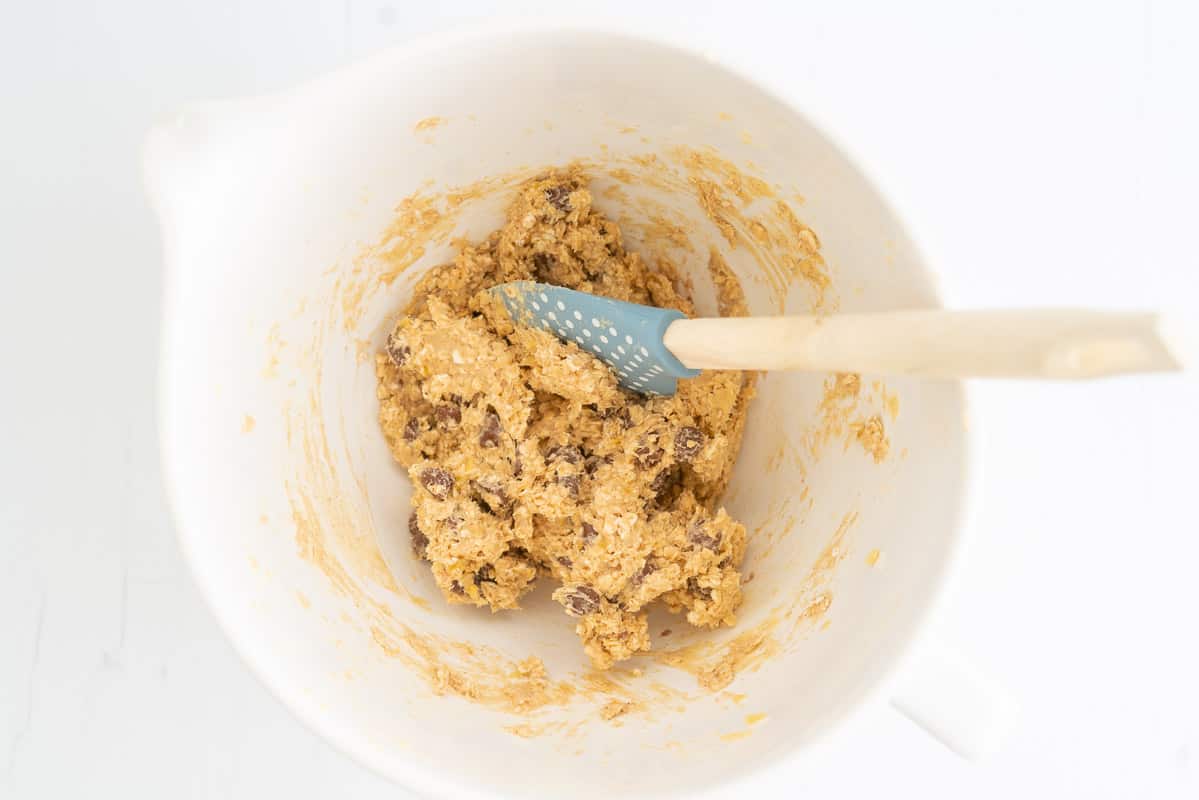 Choc Chip Oatmeal Cookie Dough in a mixing bowl with a blue spatula.