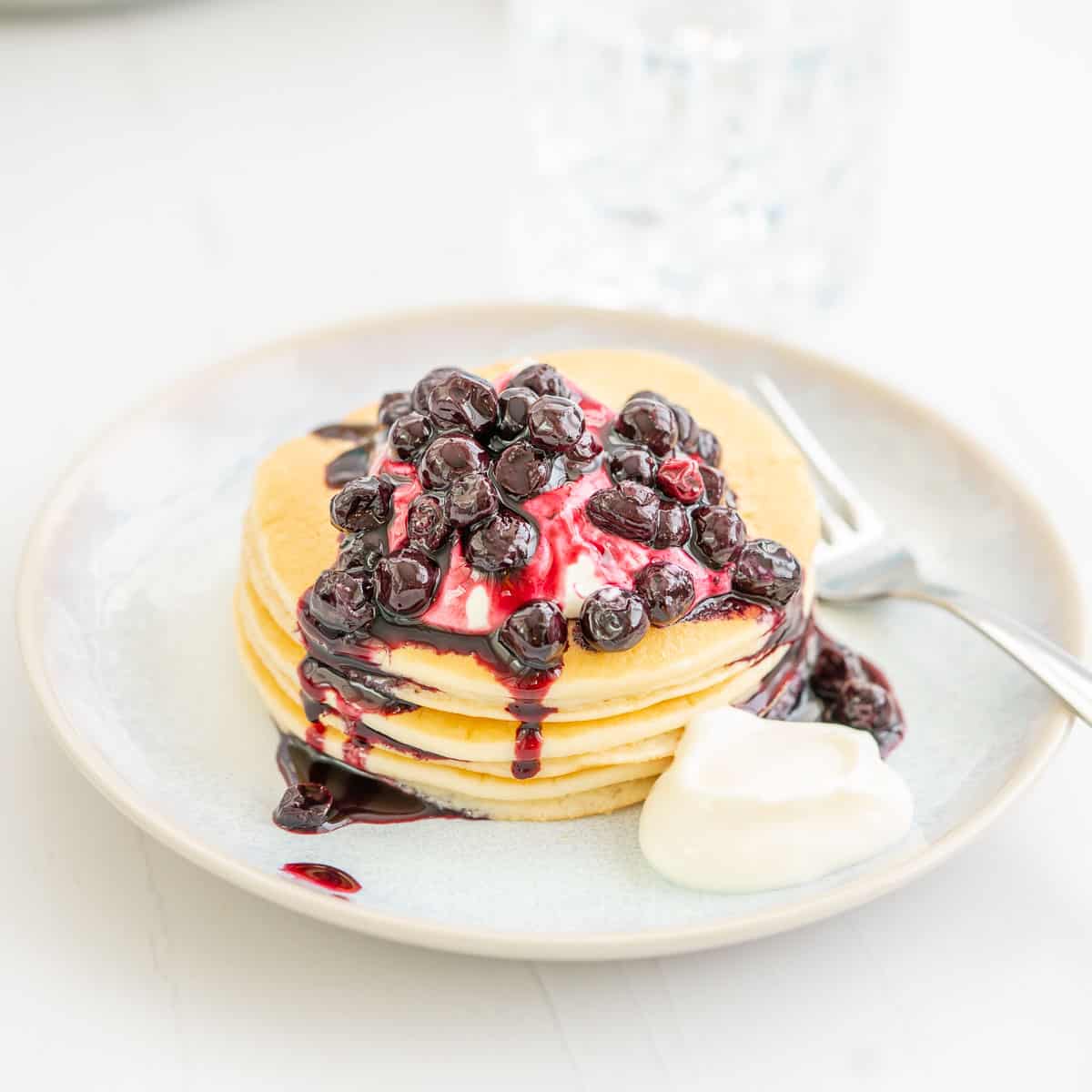 A short stack of pancakes drizzled with blueberry compote and yoghurt.