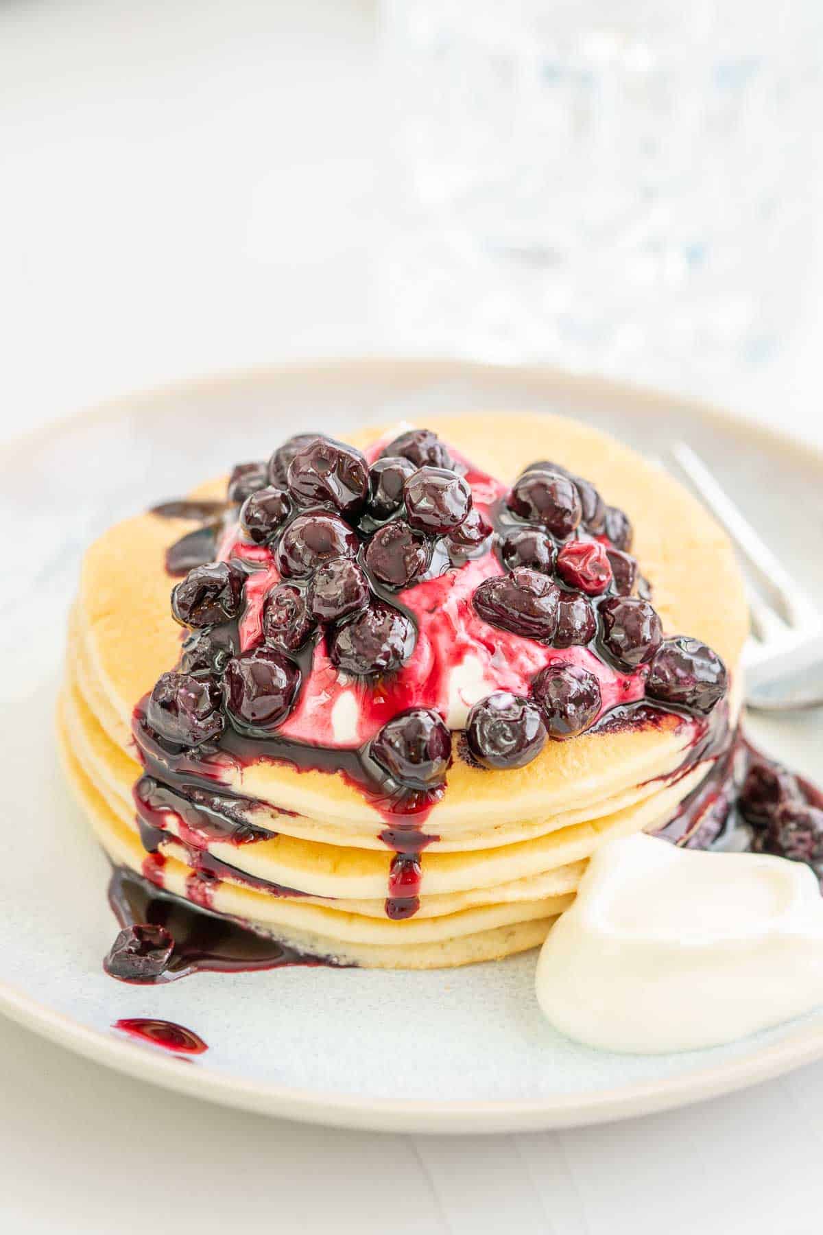 A short stack of pancakes drizzled with blueberry topping and yoghurt.