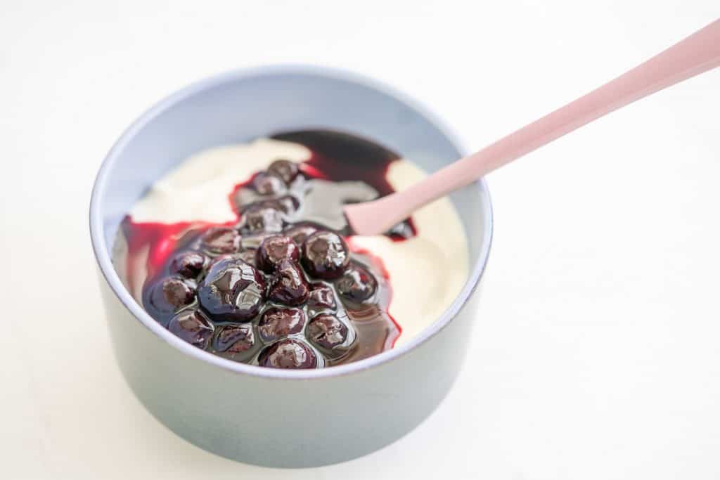 A small blue bowl filled with greek yoghurt topped with blueberry compote.
