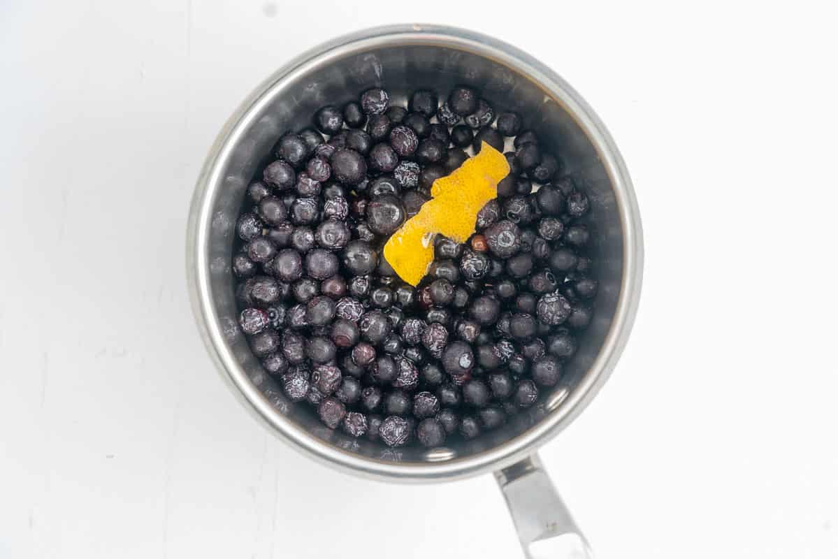 Frozen blueberries and a strip of lemon zest in the bottom of a small saucepan.