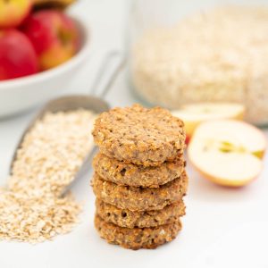 A stack of 5 oatmeal toddler cookies on a bench top with rolled oats and apples in the background.