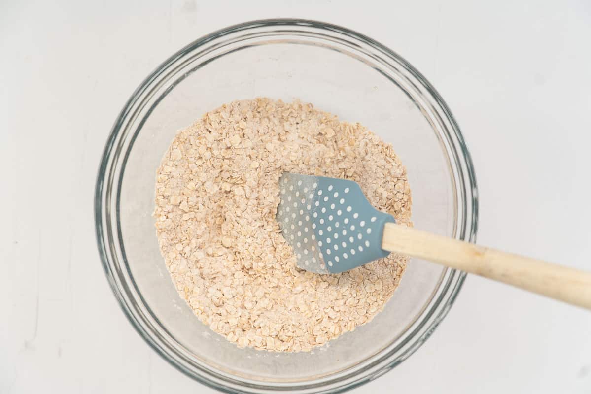 Dry ingredients in a glass mixing bowl with a blue polka dotted spatula.
