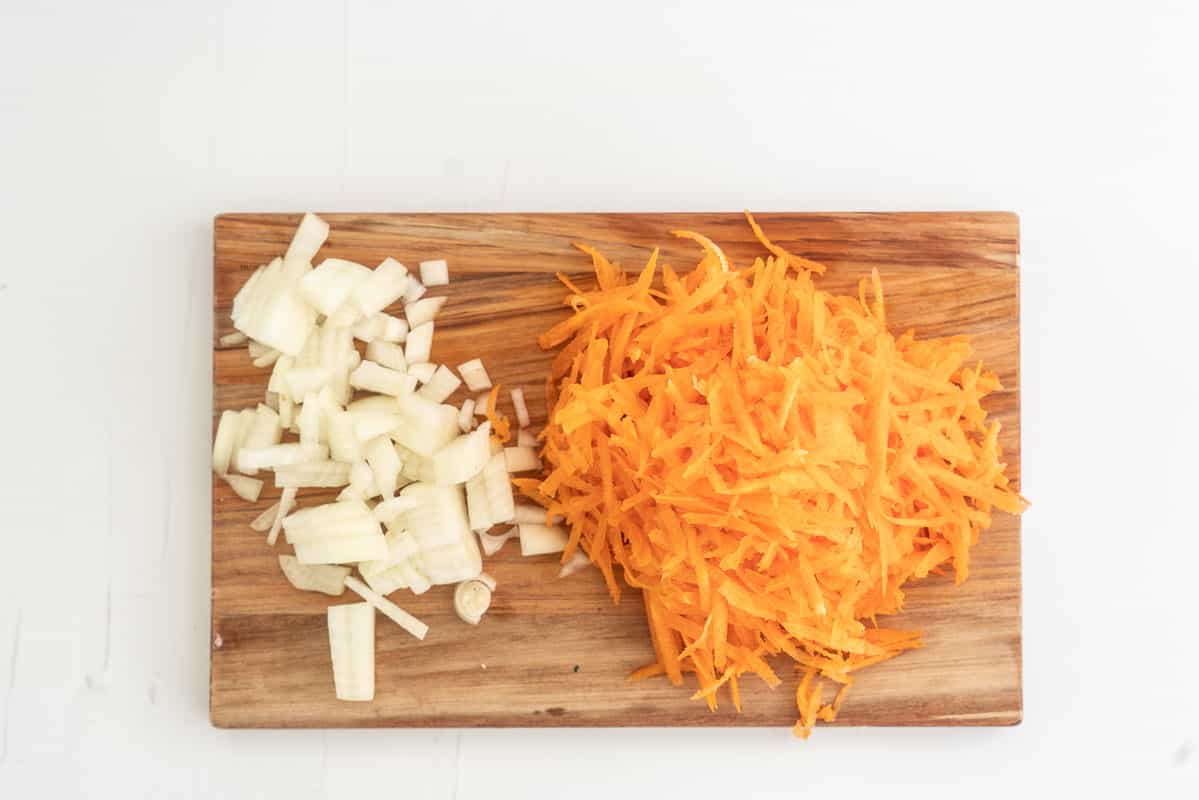 Diced onion and grated carrots on a wooden chopping board.