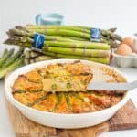 A slice of quiche on a serving spatula sitting on top of the remaining quiche,