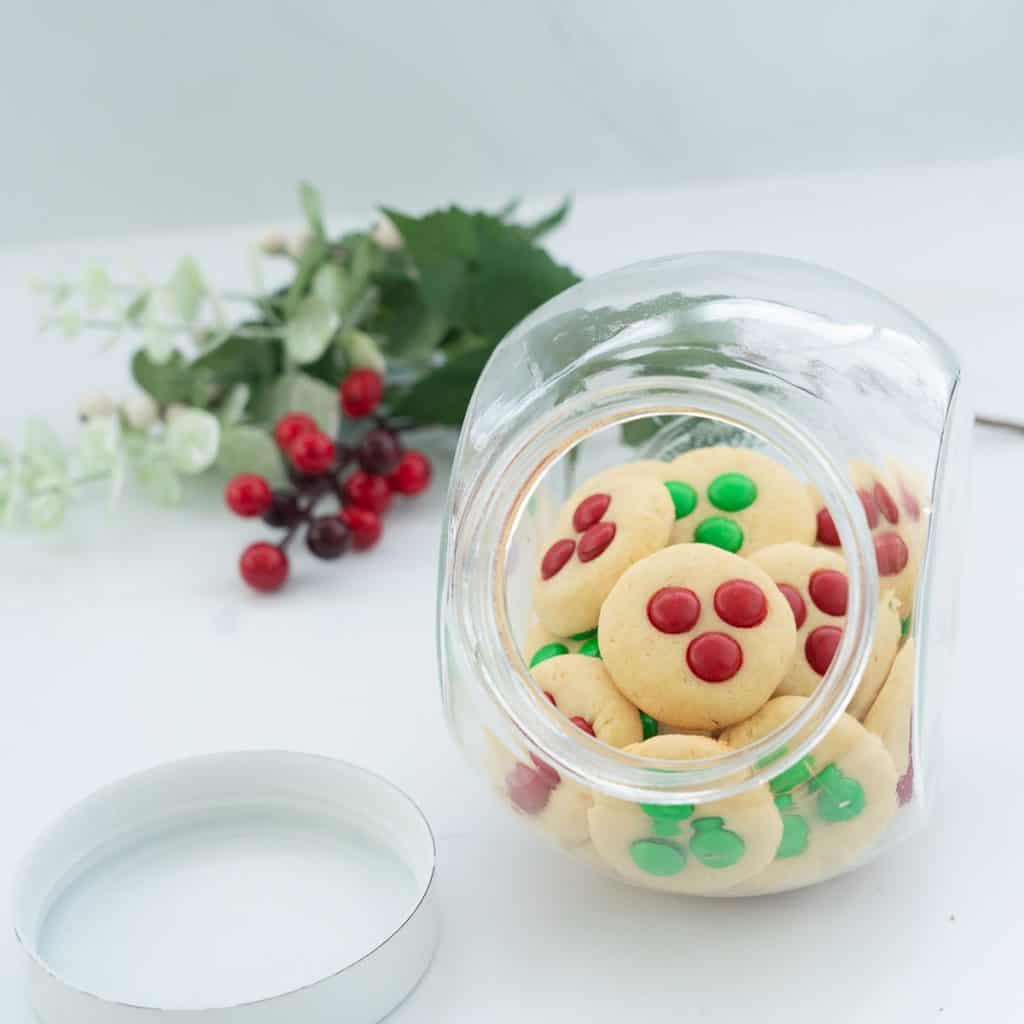 A glass cookie jar filled with red and green candy decorated Christmas cookies.
