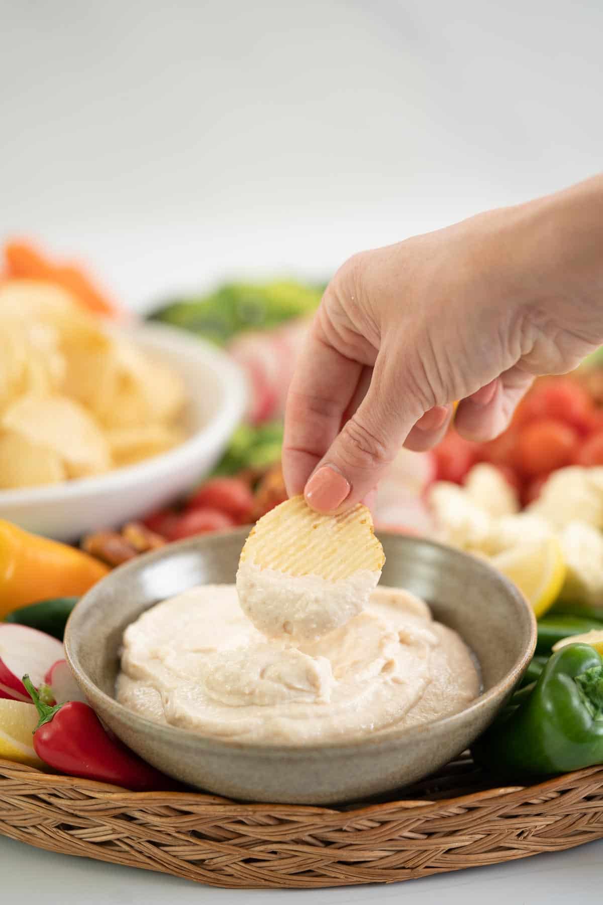 A hand holding a chip loaded with dip above a bowl of kiwi onion dip.