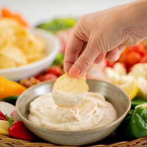 A hand holding a chip loaded with dip above a bowl of kiwi onion dip.
