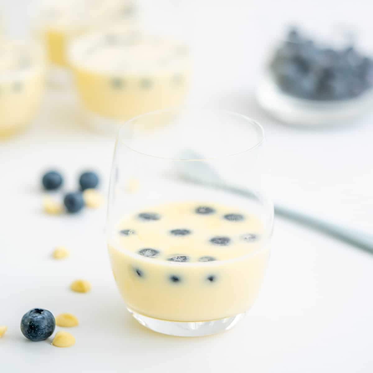 A glass of white chocolate mousse with blueberries floating on the surface.