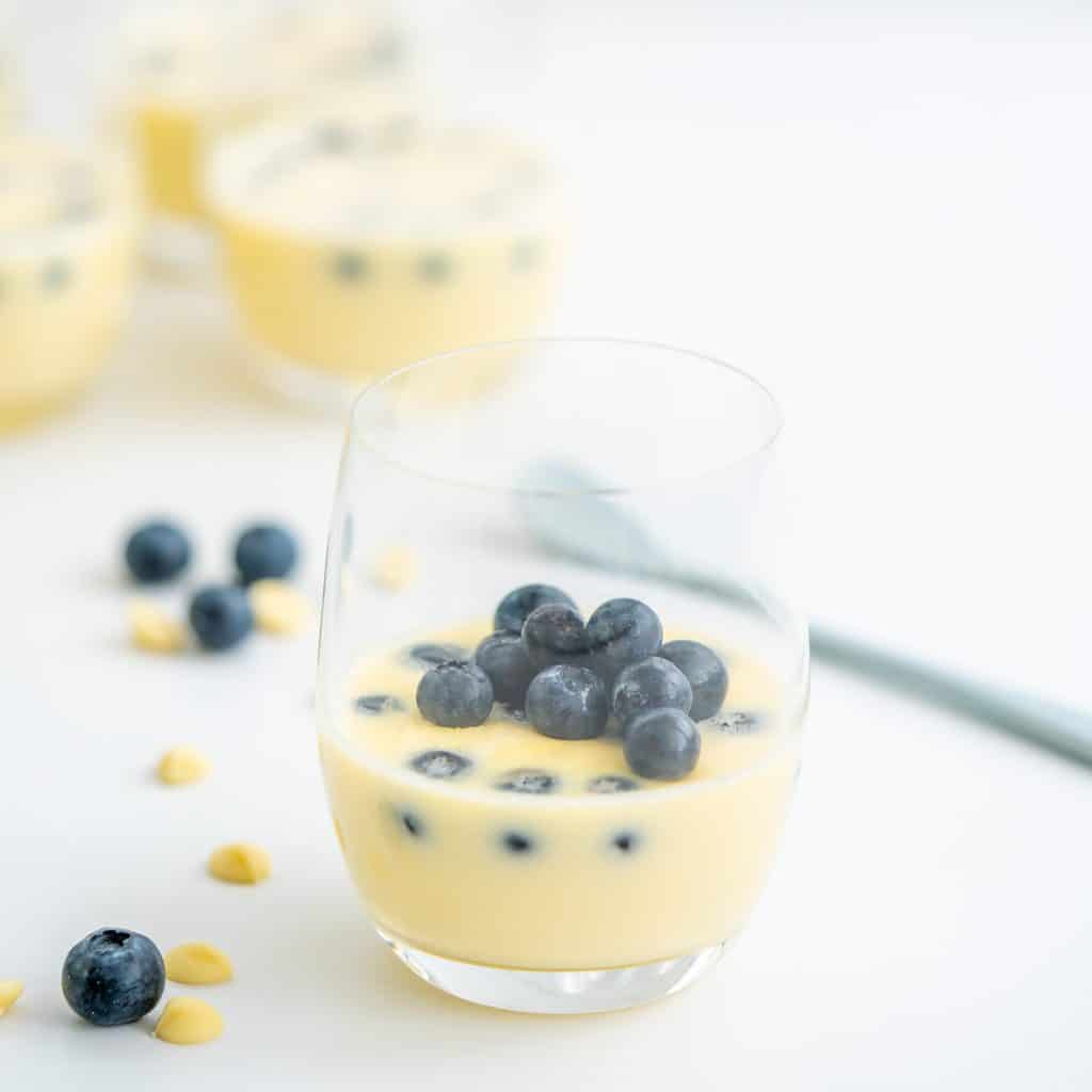 A glass filled with white chocolate mousse garnished with fresh blueberries