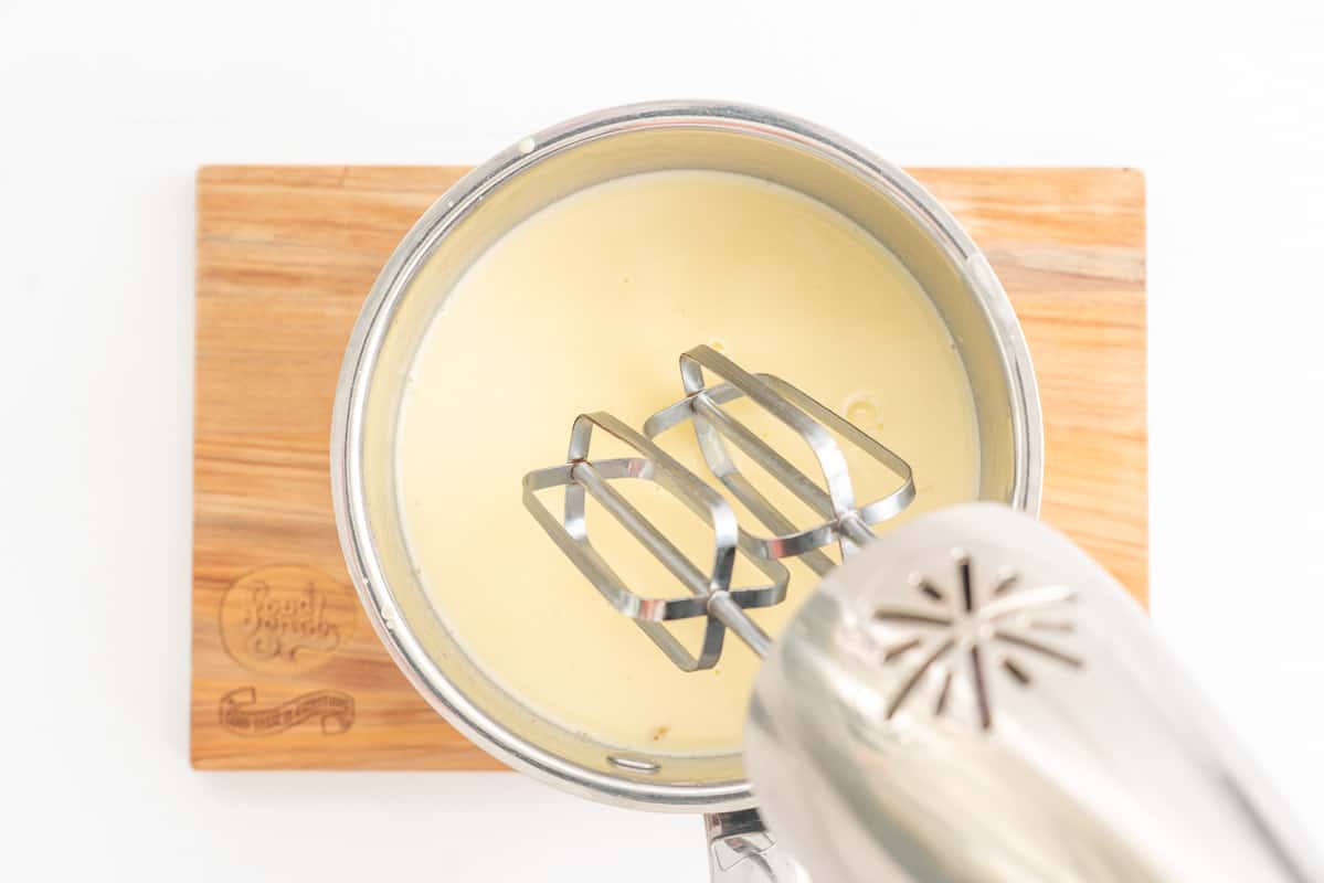 An electric beater being held above a saucepan of warmed cream.