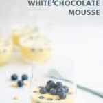 A glass filled with white chocolate mousse garnished with fresh blueberries with text overlay.