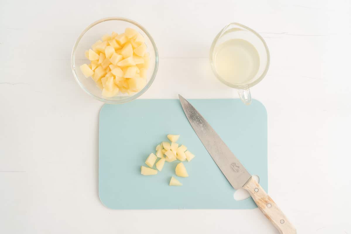 Light blue chopping board and knife, diced pears in a glass bowl with pear juice in a second bowl.