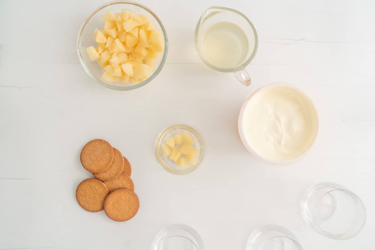 A glass with cubes of pears in the bottom, surrounded by more pears, cookies and yogurt.