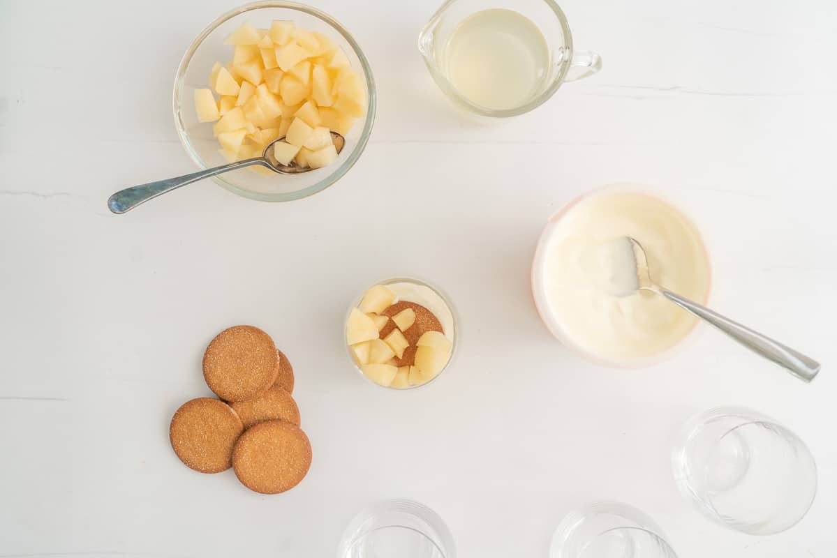 A glass with cubes of pears, gingernut biscuit and yogurt  in the bottom, surrounded by more pears, cookies and yogurt. 
