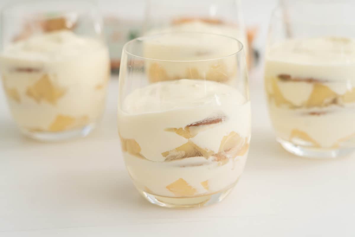 four glases filled with layers of pears, cookies, and yoghurt. 