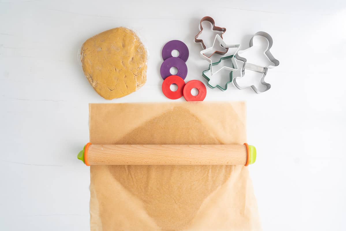 Cookie dough being rolled out between two pieces of brown parchment paper, with a wooden rolling pin.