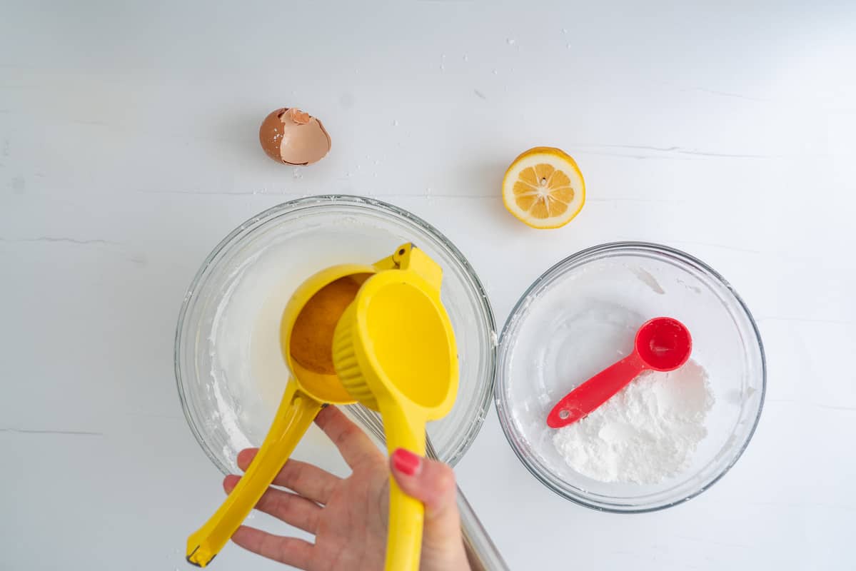Lemon juice being squeezed into a bowl of royal icing using a yellow lemon squeezer. 