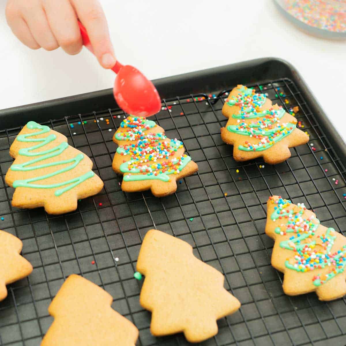 Christmas tree shaped cookies decorated with green zig zags of royal icing, topped with colourful sprinkles. 