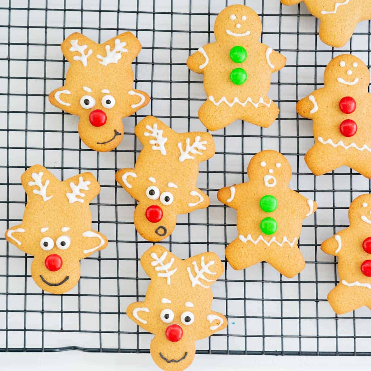 Reindeer cookies and gingerbread man cookies on a cooling rack. They are decorated with white royal icing and red an green candy.