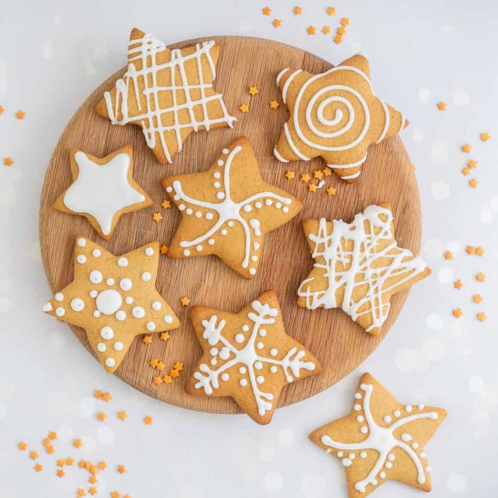 Star shapes gingerbread cookies decorated with different patterns of white royal icing on a round wooden serving board.
