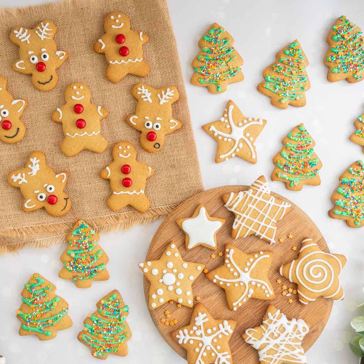 A selection of decorated gingerbread cookies laid out on a counter top, shapes include stars, reindeer, gingerbread men and Christmas trees.