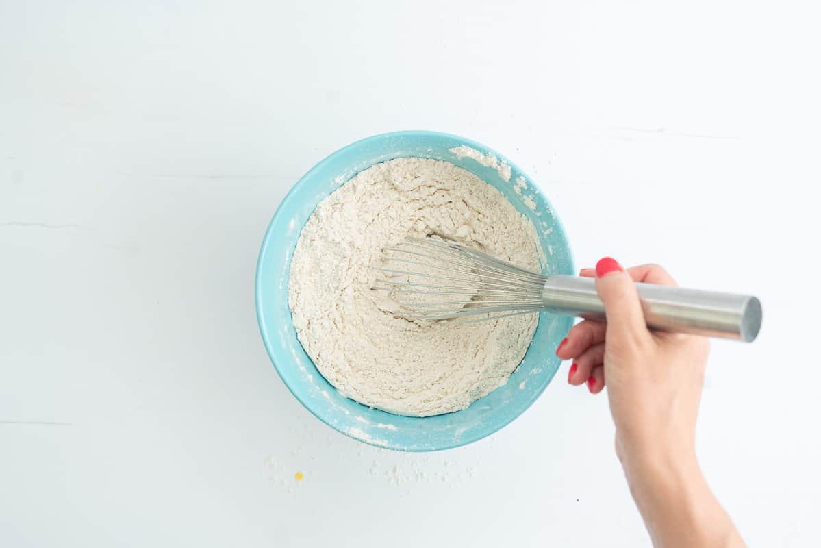 A hand whisking dry ingredients in a light blue mixing bowl.