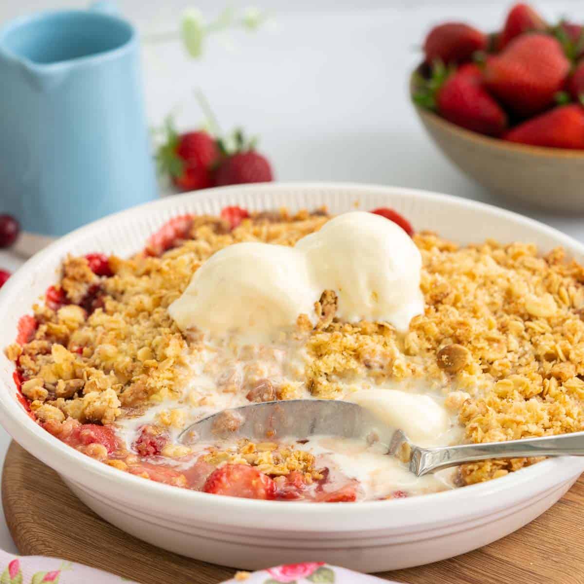A large serving spoon dishing out strawberry crumble topped with icecream.