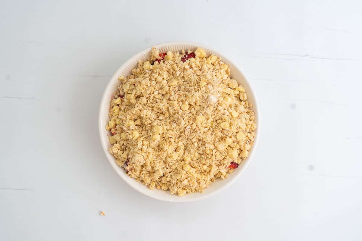 A pie dish with a strawberry crumble ready to go into the oven.