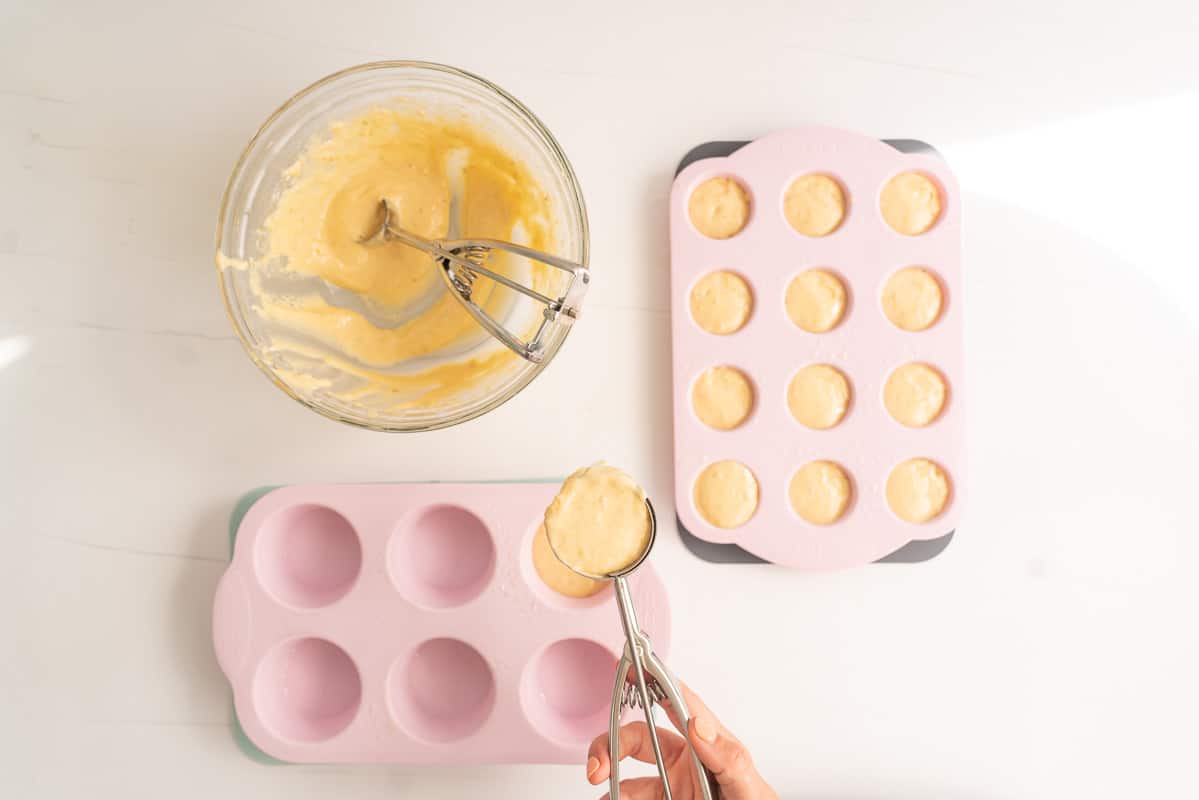 Muffin batter being portioned into pink silicone muffin cases.