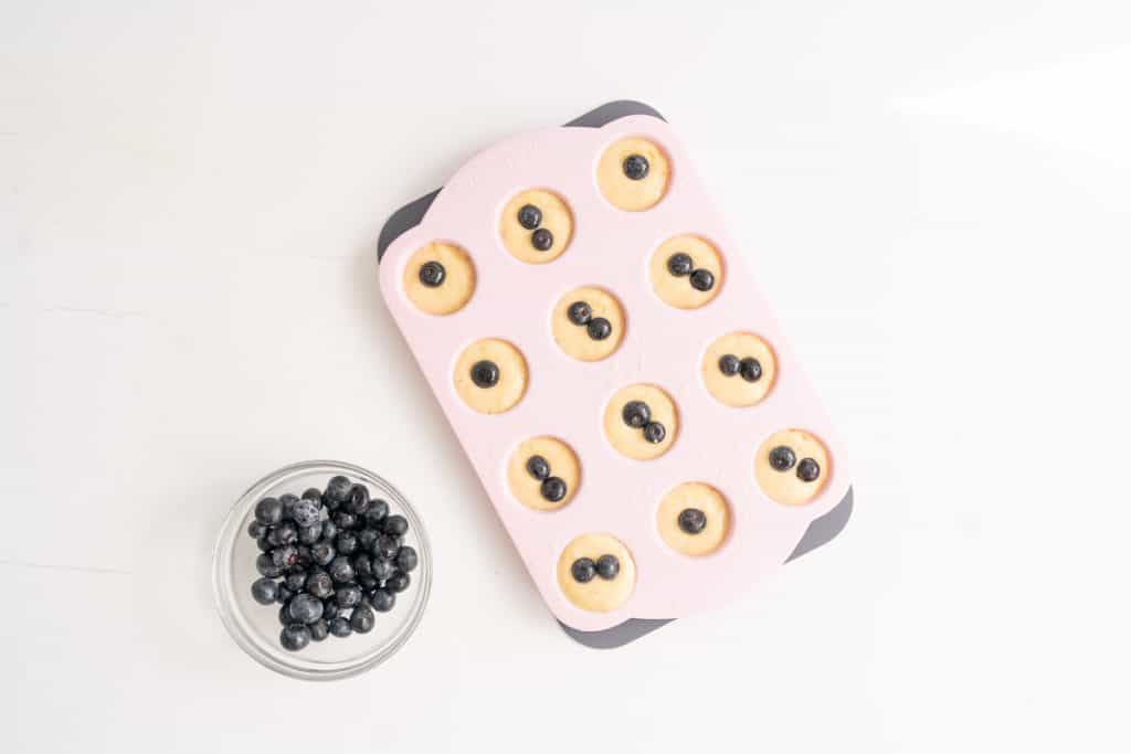 Mini muffins in a pink silicone muffin cases, each topped with blueberries.
