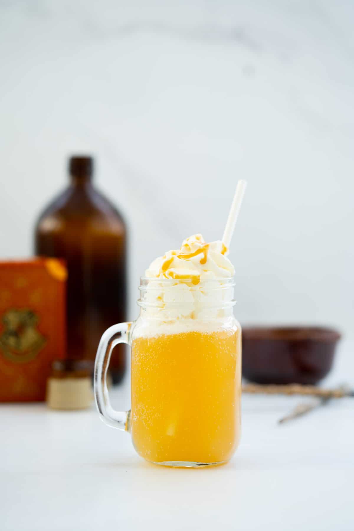 A glass beer handle filled with butterbeer and whipped cream, brown glass bottle and golden wands in the background.