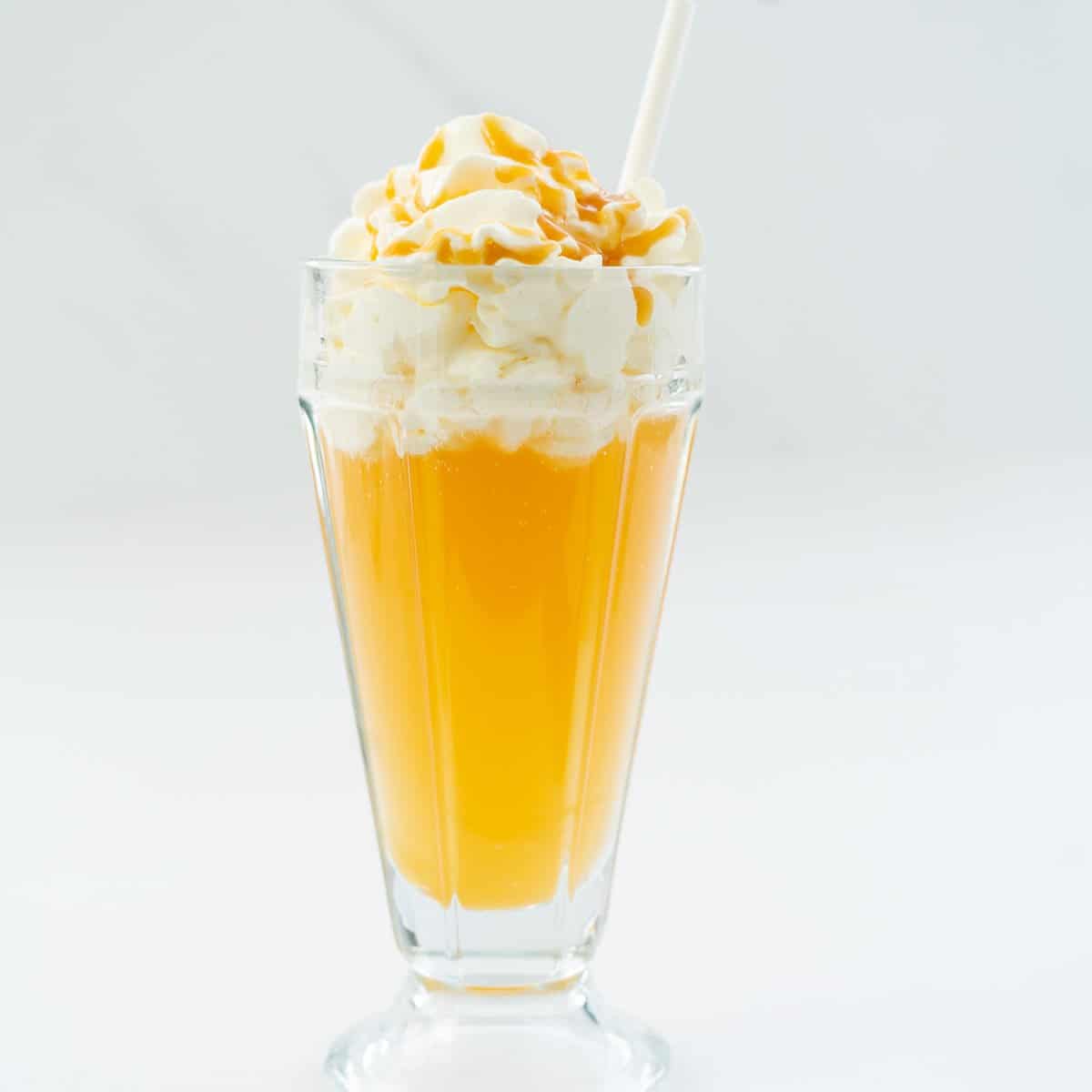 Golden butterbeer topped with whipped cream and caramel sauce in a tall ice cream sundae glass.