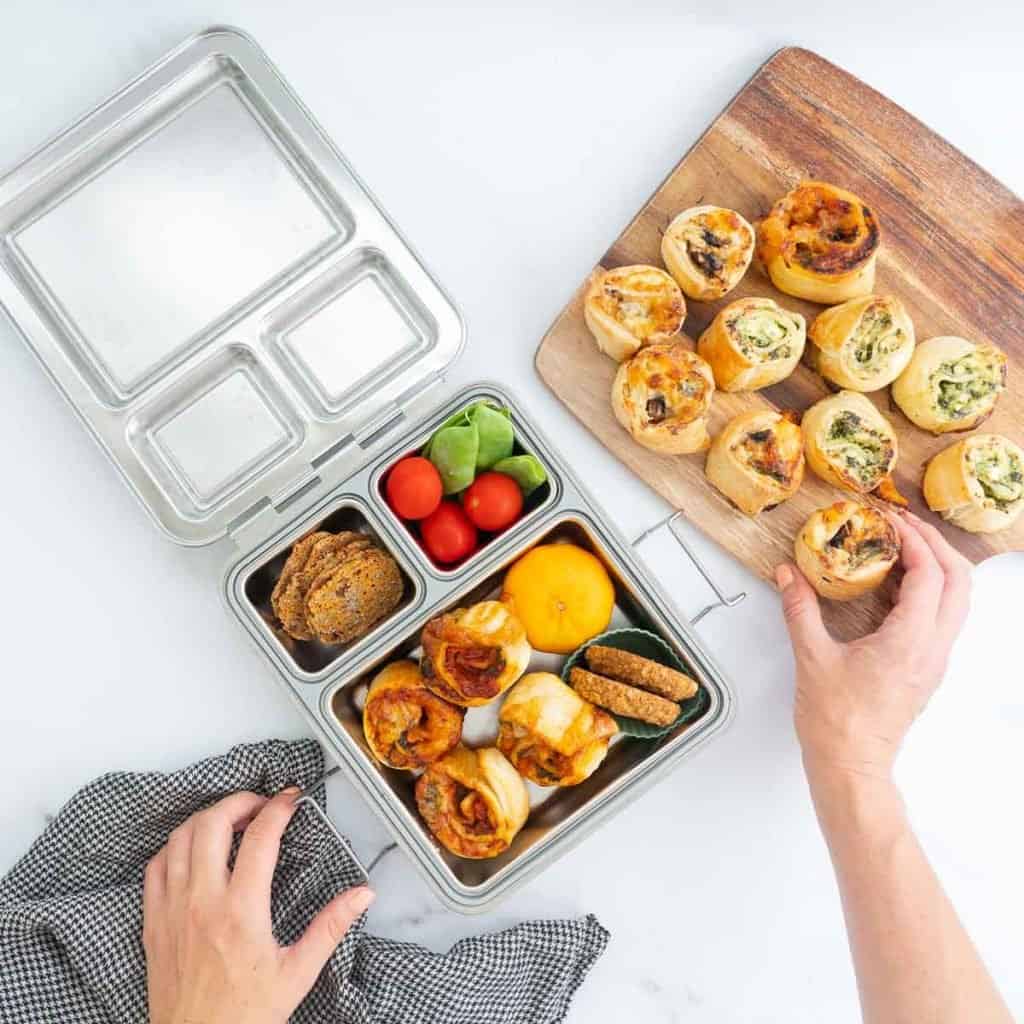 Pizza scrolls on a wooden board being packed into a stainless steel lunchbox