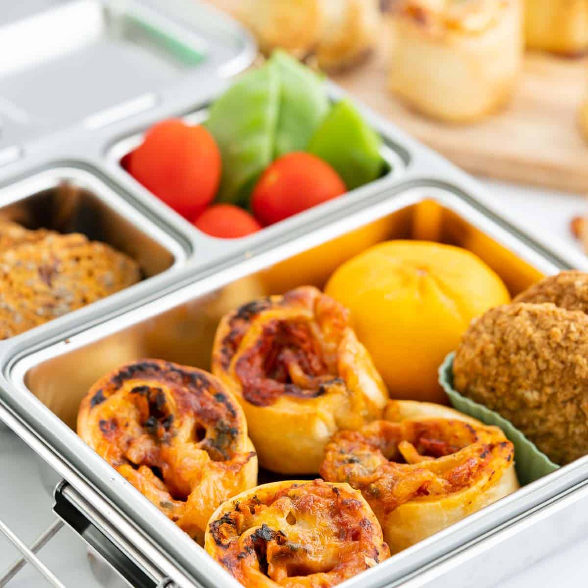 Pizza pinwheels packed in a stainless steel bento lunchbox with colourful produce.