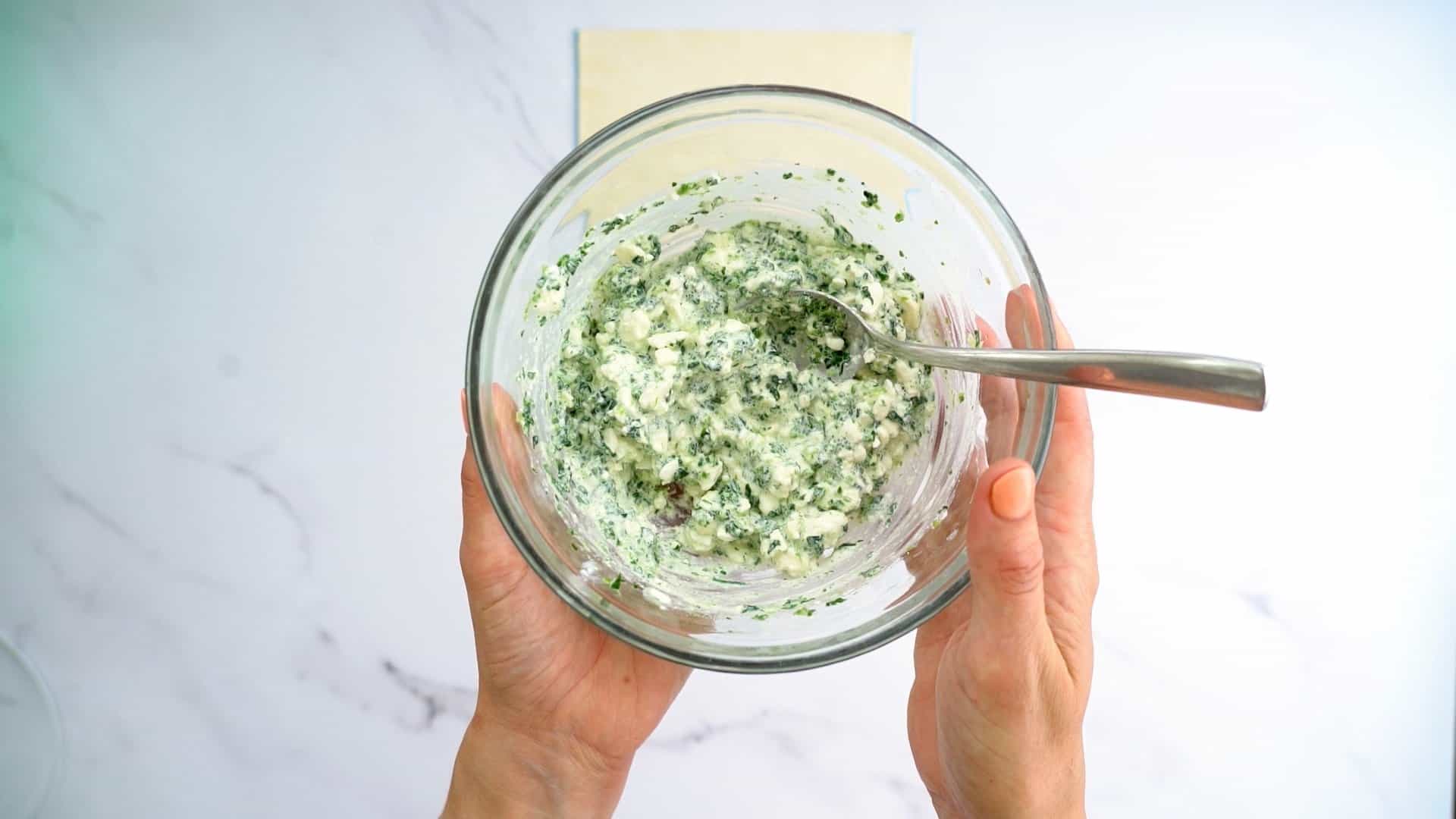 A glass bowl of cottage cheese, feta and chopped spinach combined together.