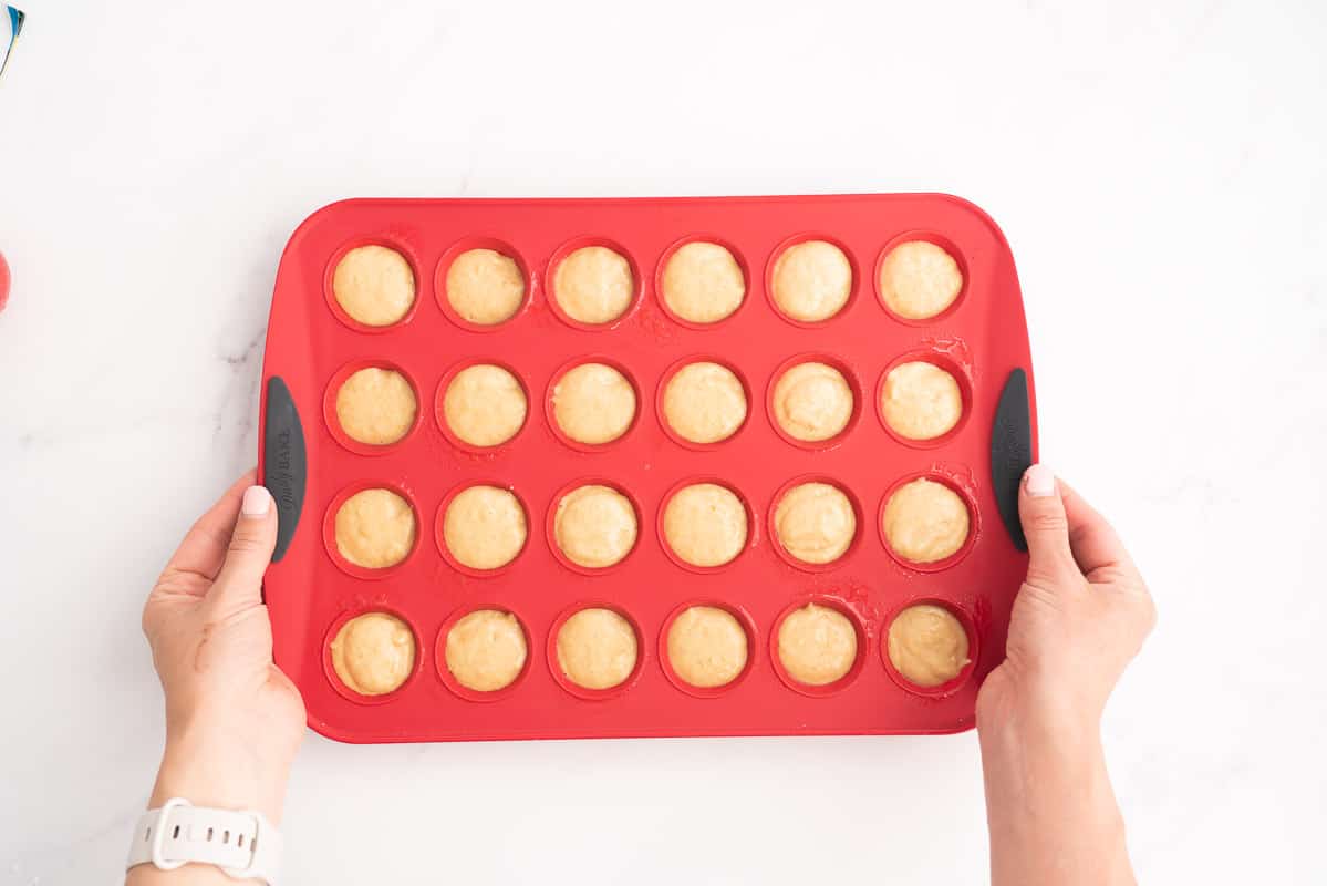 A red silicone mini muffin tray filled with portioned muffin batter.