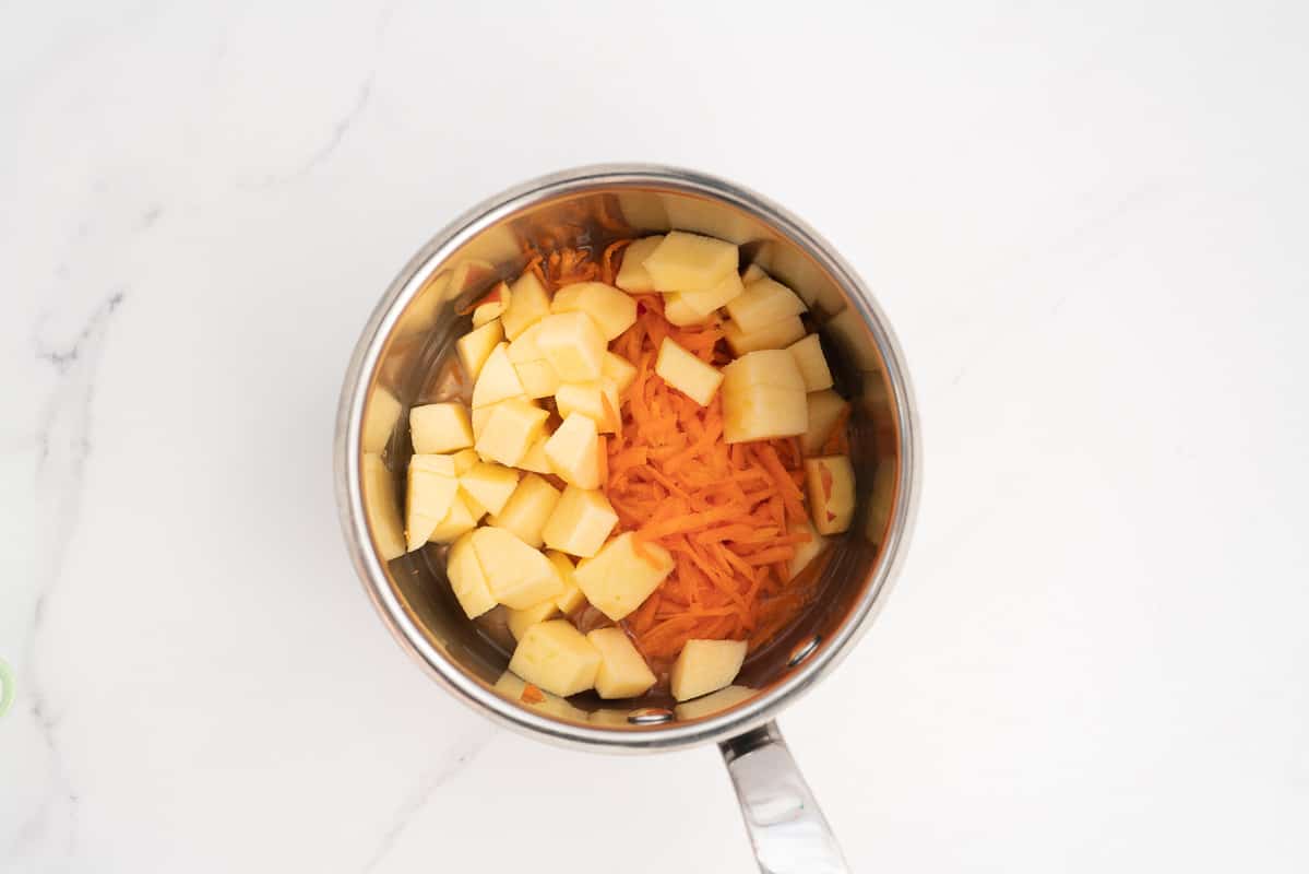 Grated carrot and cubes of peeled apple in a small saucepan.