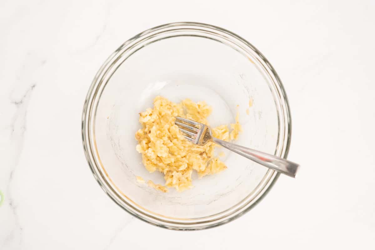 A large glass mixing bowl with mashed banana in the base.