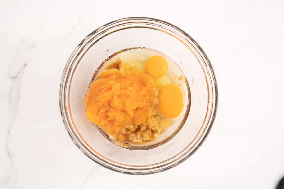 A glass mixing bowl containing fruit anfd vegetable purée, mashed banana and eggs.