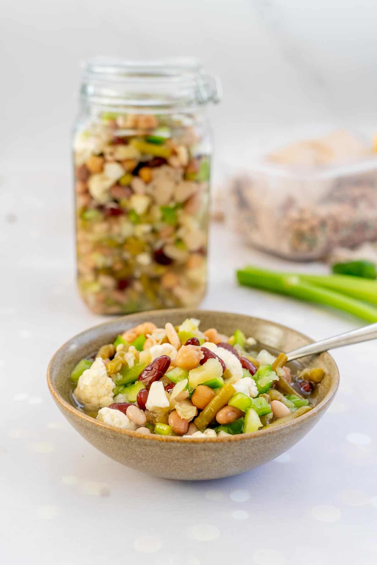 A bowl of bean salad sitting in front of a large mason jar filled with bean salad. 