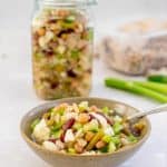 A bowl of bean salad sitting in front of a large mason jar filled with bean salad with text overlay.