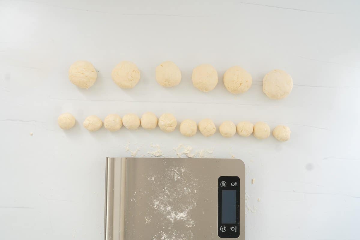 6 large and 12 small dough ba;;s on a floured bench with a set of kitchen scales