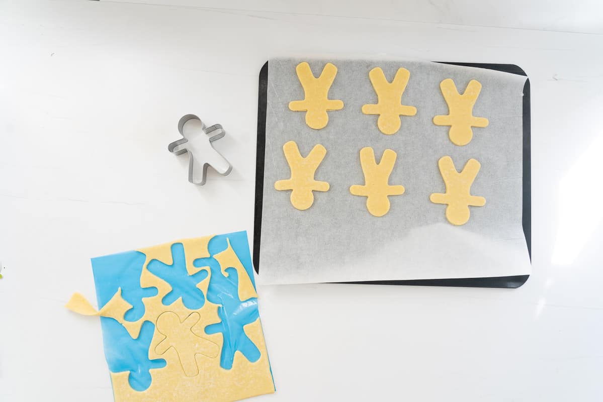 Gingerbread men being cut using a cookie cutter from a sheet of pastry.