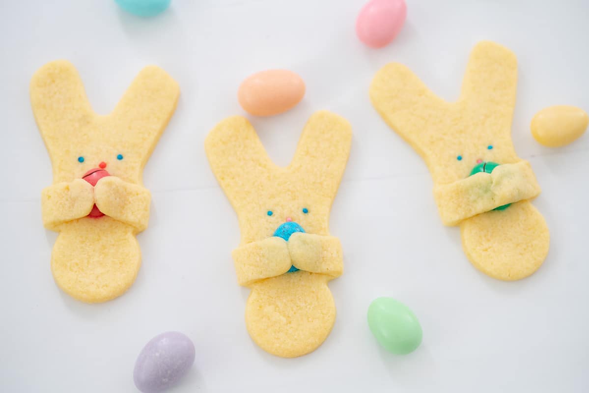 Three easter bunny cookies lying on crinkled white baking paper scattered with sugared almonds.