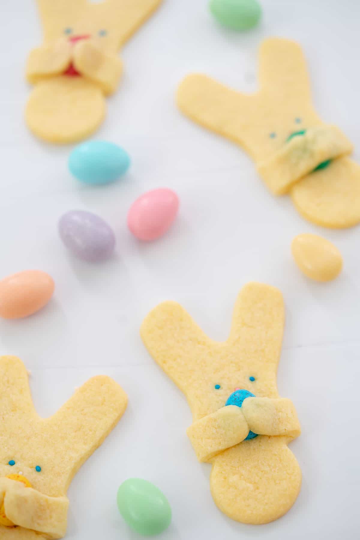 Easter bunny cookies on a white bench top scattered with sugared almonds.