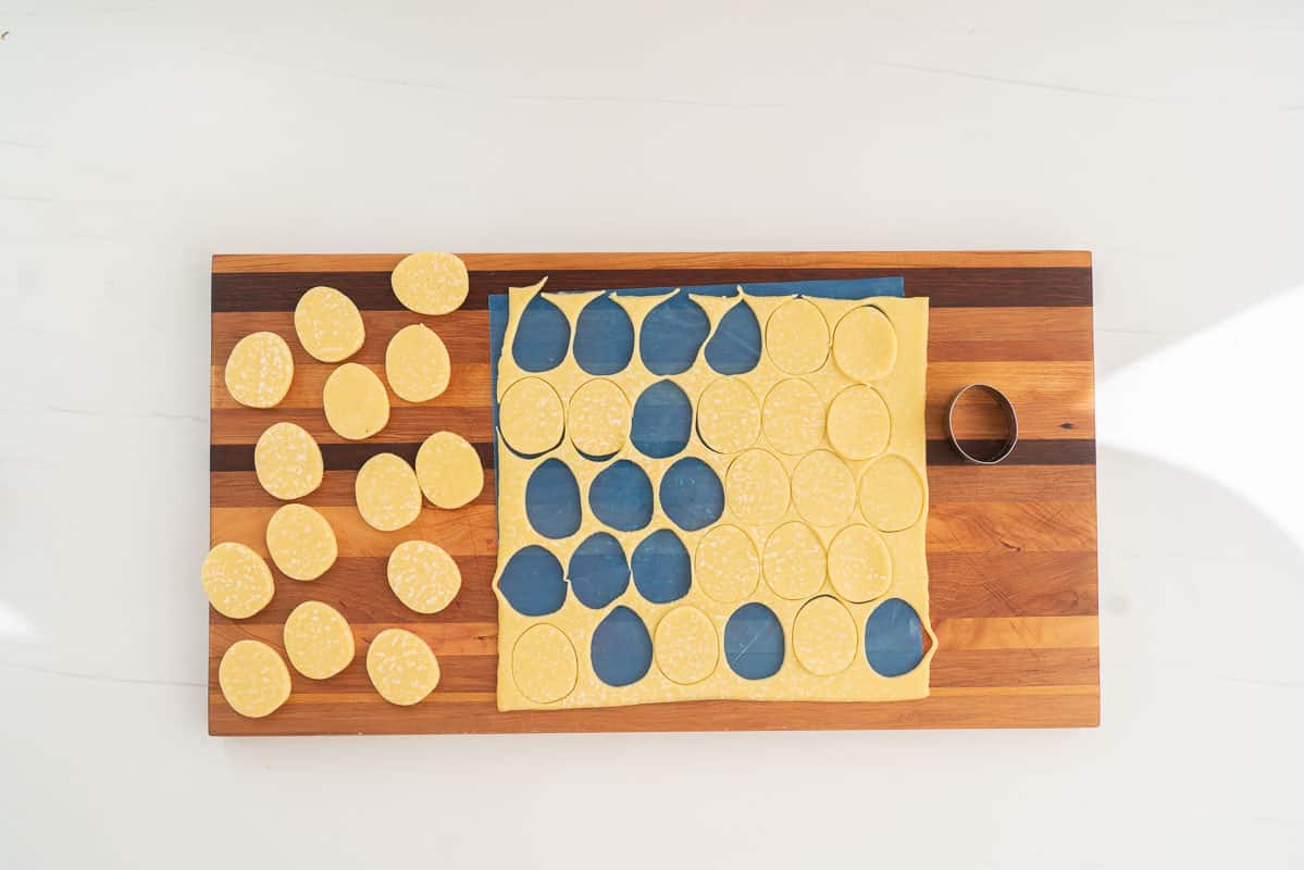 A pastry sheet on a wooden shopping board, oval shapes have been cut out of the pastry.