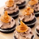 Chocolate cupcakes topped with chocolate buttercream and a caramel cupcake topper in the shape of a sorting hat from harry potter with text overlay.